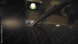 The cable slowly unwinds from a large spool at the cable factory. Close-up. A bright lamp in the background shines brightly. Production process at the cable factory. 4K