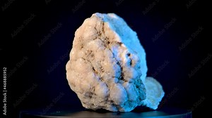 Large quartz crystal in rock on a rotating display stand. Black background and blue accent lights show off sparkling crystals in up close view.