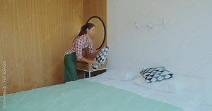 Young maid tidying up bed in hotel room, Cleaning service concept.