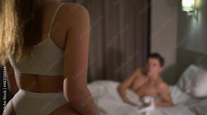 A beautiful young woman enters the bedroom, takes off her shirt and, in lingerie, lies down on the bed next to her husband.