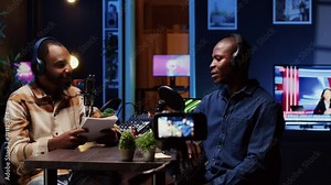 Internet show host making guest laugh, cracking jokes during comedy focused podcast. Talking show interviewer broadcasting live from living room studio decorated with neon lights