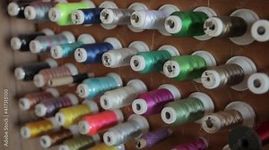 Industrial spools of colored thread for garment production and clothing repairs are kept on the booth at the booth. The coils are put on hooks. Multicolored threads on the stand in the workshop