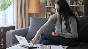 A young beautiful girl with dark hair, in a gray sweater, finishes a lesson on the computer, closes it and looks out the window. Home environment.