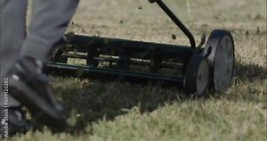 Pushing a manual mower across rough grass,