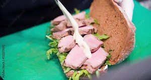 Sandwich cooking 4k video: chef puts sauce on half of sandwich, ham and bread with herbs. Food preparing in restaurant