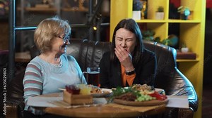 The girl is sitting with an older woman in a restaurant. They have ordered drinks and food. The girl is telling something and crying, while the older woman is comforting her.