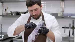 Male pastry chef, who uses a washcloth to apply shiny candurin to a mold for chocolate spheres.