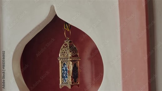 Ornate gold lantern hangs in a Moorish-style alcove. The lantern swings gently, creating a peaceful and exotic ambiance. The red clay wall and white trim add to the Moroccan feel. culture