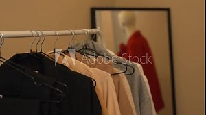 Women's clothes hang on hangers in the fitting room. There is a mirror in the background, in which a mannequin is reflected.