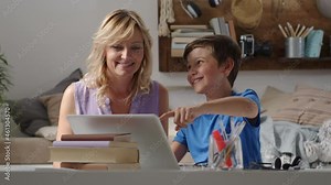 Happy family at home, mother and son have fun using computer, parent with child browsing internet on laptop, little boy student shows something pointing at the monitor