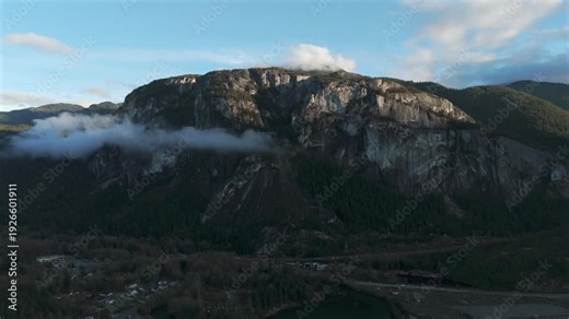 Massive Rocky Mountain Cliff Stawamus Chief Above Dense Forest With Low Clouds In Squamish, BC, Canada. wide drone shot