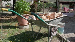 Dirty wheelbarrow with rock stones of different size and shapes, restoration works on construction site, preparing orange decorative stones for installation on wall