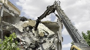 Demolition by a demolition machine. Spraying water to prevent dust formation. Damaged building.