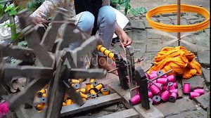 Woman spinning cotton thread by hand outside her house. The yarn is twisted into a reel through a process to make cloth.