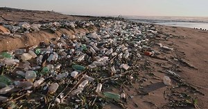 Aerial close-up fly over view of plastic pollution flowing down a river mouth into the ocean.Environmental damage to the oceans and sea.