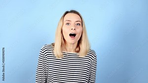 Camera view of amazed shocked young blond woman looking into camera demonstrates wow surprised face expression and call everybody to look on isolated blue background