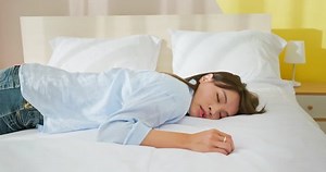 asian woman falling down and lying on bed is tired at daytime