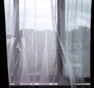 Nature view through the window. Easy swaying of tulle from the wind. A transparent curtain on the window, gently moved by the wind.