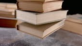 Slow motion medium handheld shot of a stack of old books falling onto...