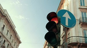 Traffic light is broken and yellow light doesn't work. Works red and switches to green. Road sign going straight. Old houses on background