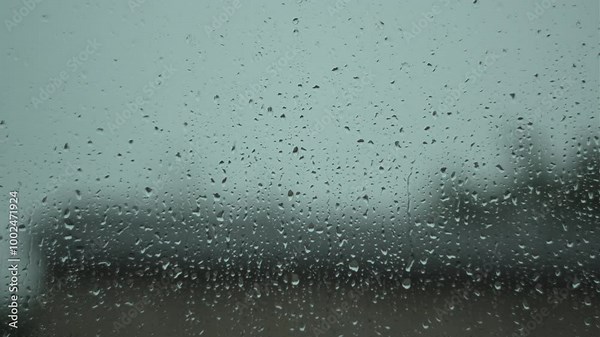 Raindrops falling on a window, streaming down smoothly, with a blurred background.