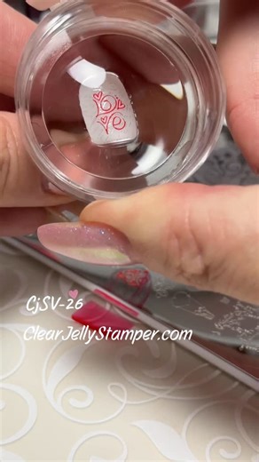 Clear Jelly Stamper on Instagram: "🩷♥️Soft script meets bold love 💖✨ This look is all about contrast — delicate white-on-white script topped with a bold, swirly LOVE that steals the spotlight in dreamy reds and pinks. Created using CjS V-26, layered with polish 034, 006 + 096 over KoKo&Claire 380, that perfect milky, white-ish base we’re obsessed with 🤍 It’s elegant, eye-catching, and surprisingly easy thanks to our layered stamping system. Two layers. Big impact. Beginner-friendly, pro-appro