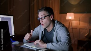 young man in eyeglasses on workplace at home, has online video call with coworkers using laptop. male applicant pass online interview using web cam. student on examination of online education.