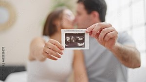 Beautiful couple holding baby ultrasound kissing at bedroom