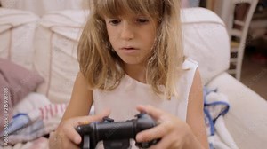 A cute little girl at home, playing with a controller (joysticks and keypad) in front of a computer screen, learning how to use it.
