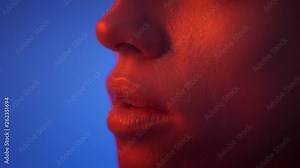 Close-up slide shot in profile of fashion model face watching seriously upwards in red neon light on blue background.