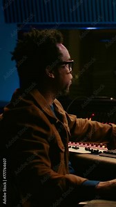 Vertical Video Tracking engineer processing and mixing sounds in control room with audio console and professional editing software on computer. Music production expert uses motorized faders and knobs