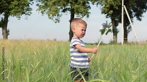 child boy kid playing with windmill pinwheel outdoors in green wheat field, celebrating usa Independence Day of America, 4th July holiday, pinwheel colors of usa flag, red blue Stars and Stripes