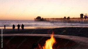 Campfire pit by Oceanside pier, California USA. Camp fire burning on ocean beach, bonfire flame in cement ring place for bbq, sea water waves. Romantic evening twilight sky, dusk after summer sunset.