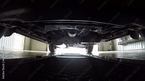 Car pulls parking into garage on metal grid, view on bottom of car. Enlarged plan of passenger car frame, trim elements, exhaust system. Elements of fuel system, exhaust pipe with muffler, equipment.