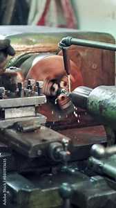 A worker controls the process of drilling a hole in a part on a lathe using coolant for cleanliness processing of surface. Close-up.