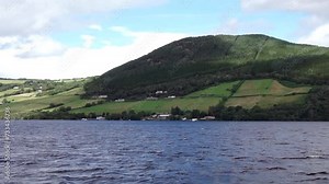 First person view. Sailing on Loch Ness, Scotland, with side views of the loch and a green hill.