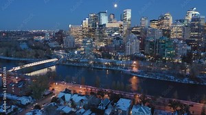 Aerial: Establishing shot of the Calgary city skyline at night. In the foreground is the Peace Bridge & the Bow River