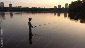 child catching fish with fishing rod from river bank at sunset. preschool boy fishing, standing knee-deep in water. Warm summer evening, little fisherman, happy childhood, favorite hobby is fishing