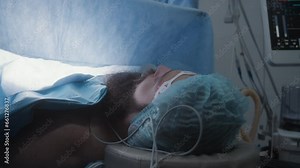 Close up of male patient lying on table under anesthesia with breathing tube during surgery. Professional surgeons operate adult man. Modern equipment in operating room. Medics save life in hospital.