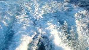 Overhead view of swirling sea water caused by a ship's propellers, as it travels along ahead in slow-motion.