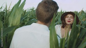 Beautiful couple in the corn field. slow motion. Follow me shot of young woman in brown hat pulling her boyfriend across cornfield.