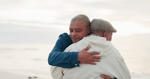 Senior father, man and hug at beach with love, care and bonding on vacation, holiday or travel outdoor at sunset. Elderly dad, adult son and embrace at ocean, sea and happy for family time together
