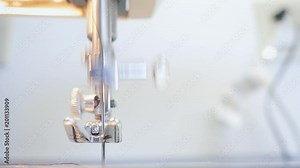 Closeup of a sewing machine stitching in 4k. A seamstress works the electric embroidery equipment as the needle goes up and down pulling the blue thread through textile fabric.