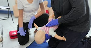 Closeup man learning how to make chest compressions on a baby dummy during the first aid group training indoors.