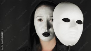 Brunette woman with white theatrical mask and make-up on her face. Sad girl takes off the theatrical mask from her face and looks at the camera. Hide emotions. High quality 4k footage