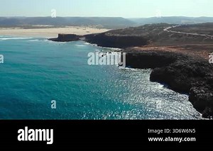 aerial panorama coastline and sandy bay, headland cliffs meeting turquoise ocean, shimmering surf and long . Media