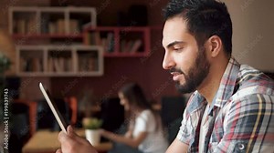 Good-looking fit man using tablet, having time off in modern european cafe, smiling joyfully as relaxing with newest technological gadget