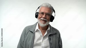 Stylish emotional old man with a gray beard and headphones listens to modern music and dances on a white isolated background. Slow motion