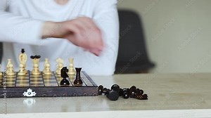 A person plays a wooden block stacking game, carefully removing a block from a tall tower