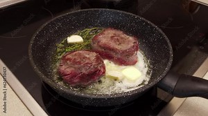 Filet mignon is fried in a frying pan in butter with garlic and thyme